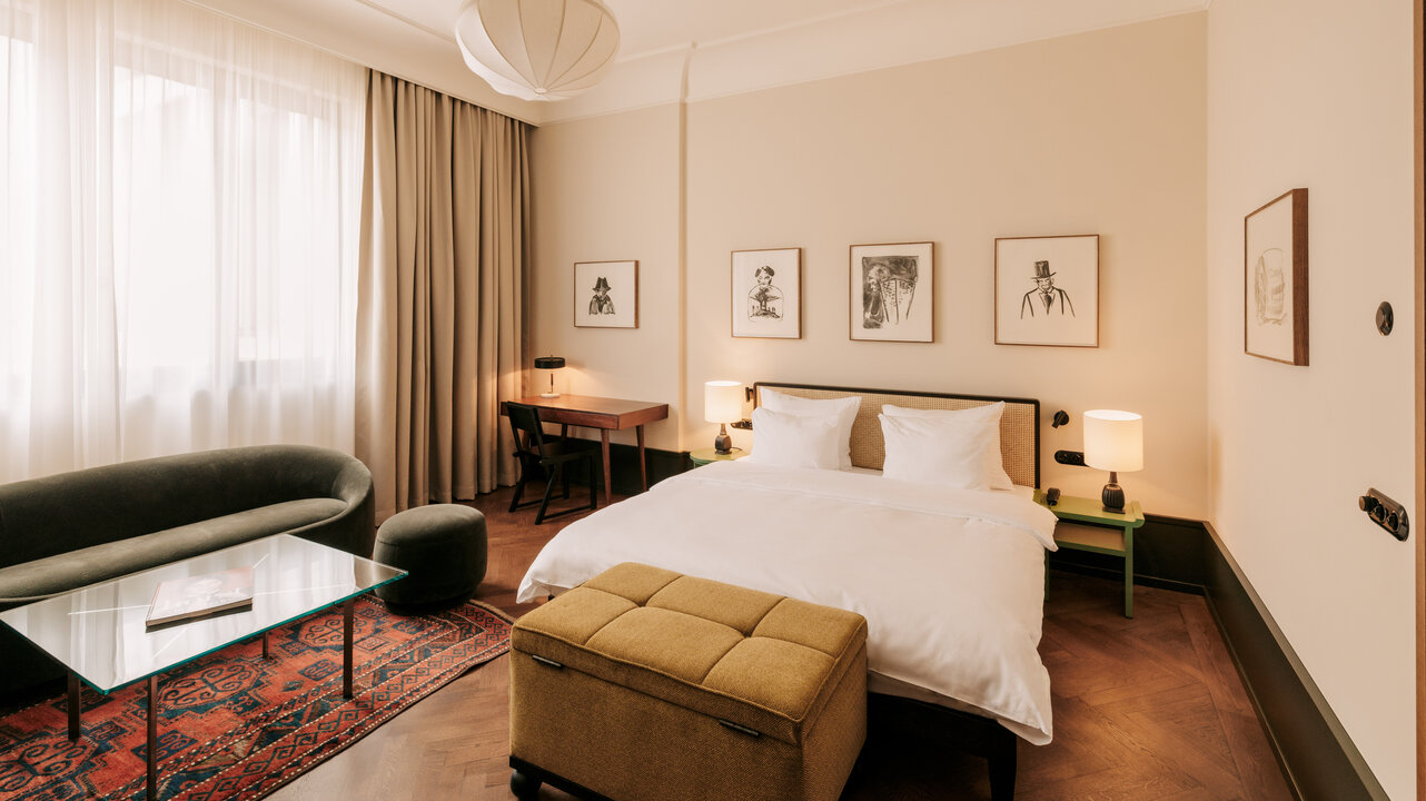 Ansicht einer Junior Suite im Château Royal Berlin, mit einem großen Bett, einer Couch und Kunstwerke von Paloma Varga Weisz.
