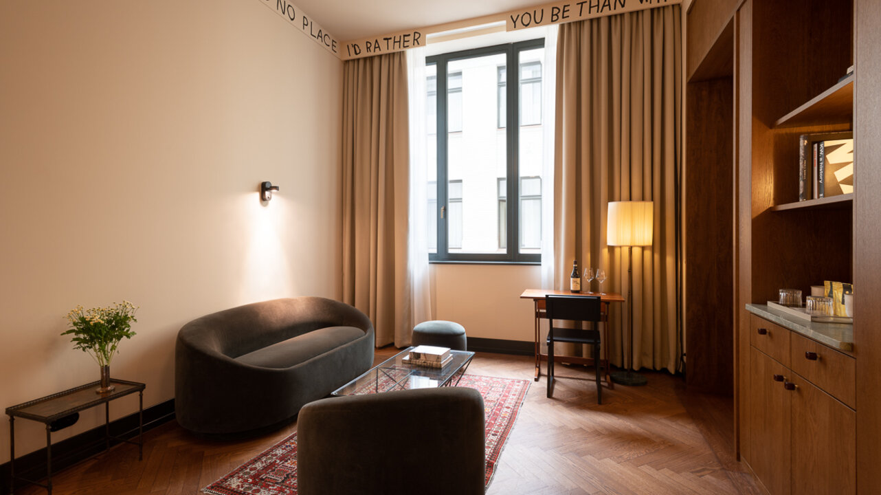 The living area of ​​a junior suite at the Château Royal Berlin with a dark couch and art by Karl Holmqvist.
