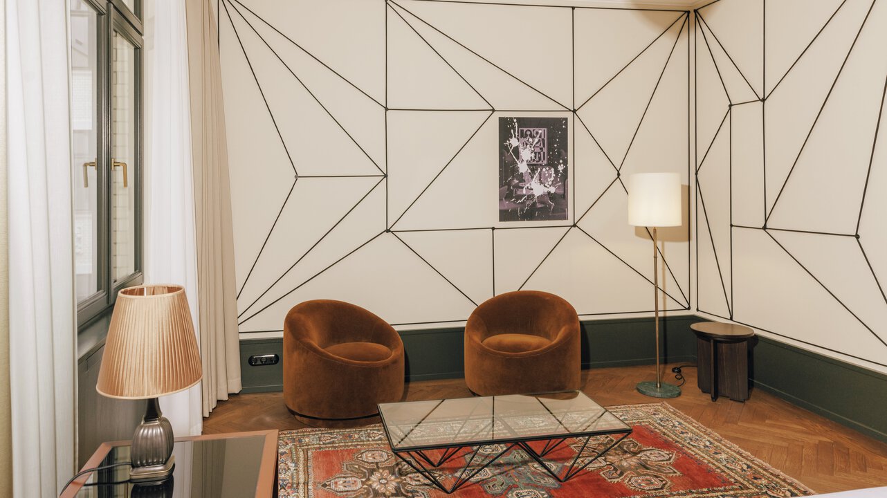 Der Wohnbereich einer Junior Suite im Hotel Château Royal Berlin mit zwei braunen Sesseln und Kunst von Julian Göthe.
