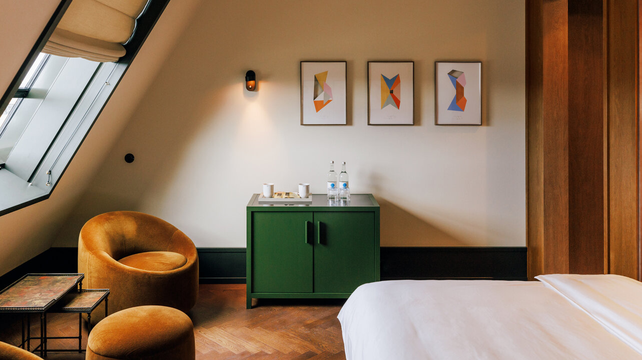 Blick auf das Bett, den Sessel und die Kunstwerke von Jorinde Voigt in einer Junior Suite des Château Royal Berlin.