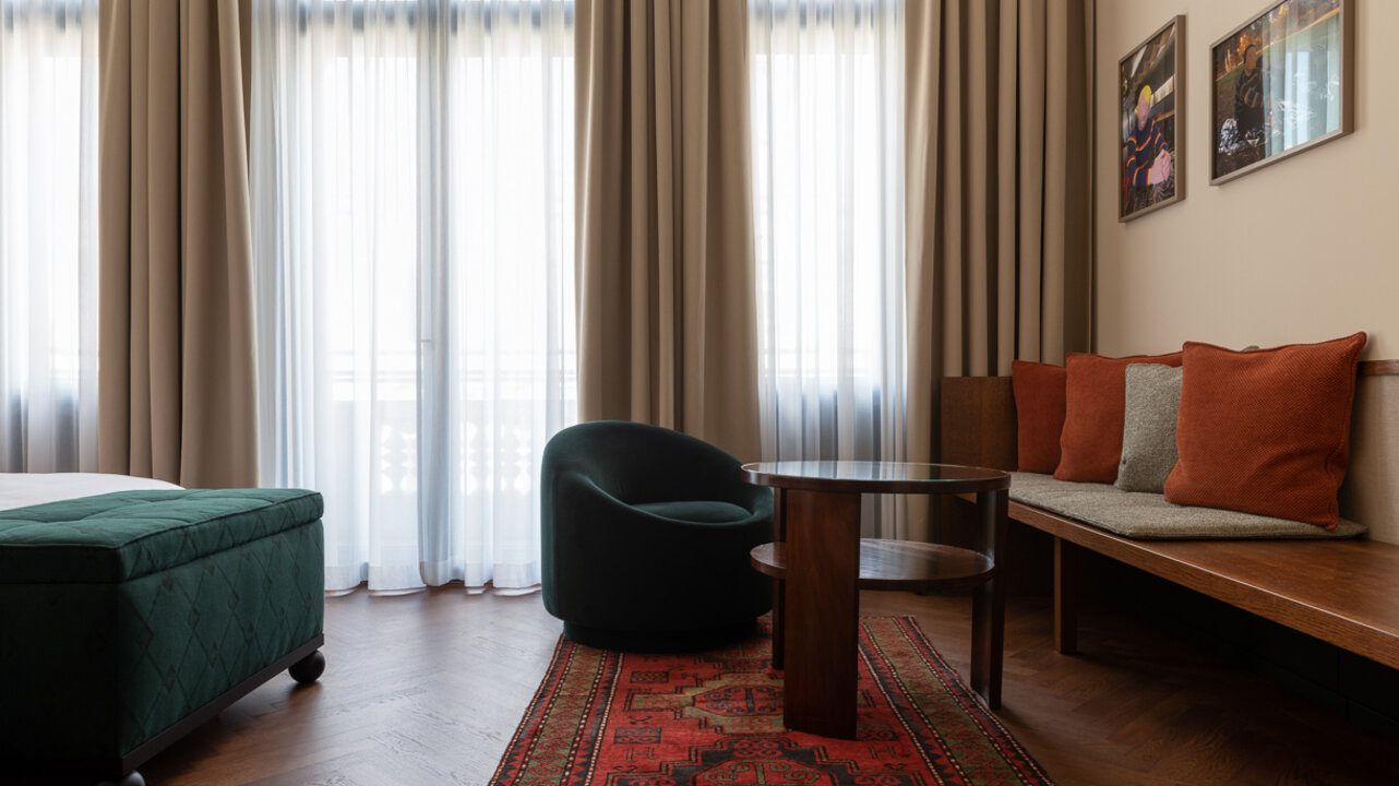 Die Sitzecke in einem großen Hotelzimmer im Château Royal Berlin mit einer Fensterwand und Kunst von Marc Brandenburg.