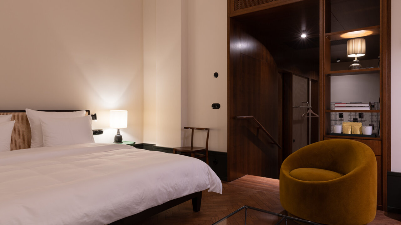Ansicht eines gemütlich eingereichteten Maisonette-Zimmers im Hotel Château Royal Berlin mit einem großen Bett und einem Sessel.