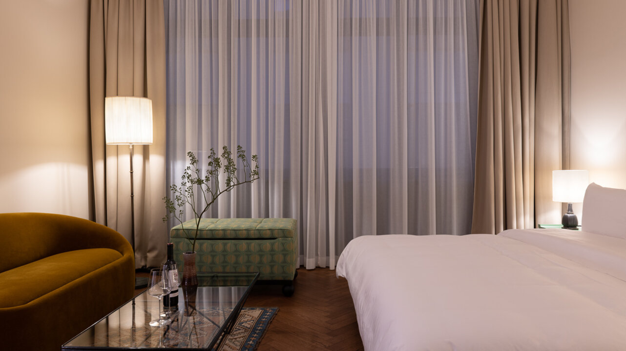 Der Schlafbereich in einem Maisonette-Zimmer im Château Royal Berlin mit einem großen Bett, einer Couch und heller Festerfront.