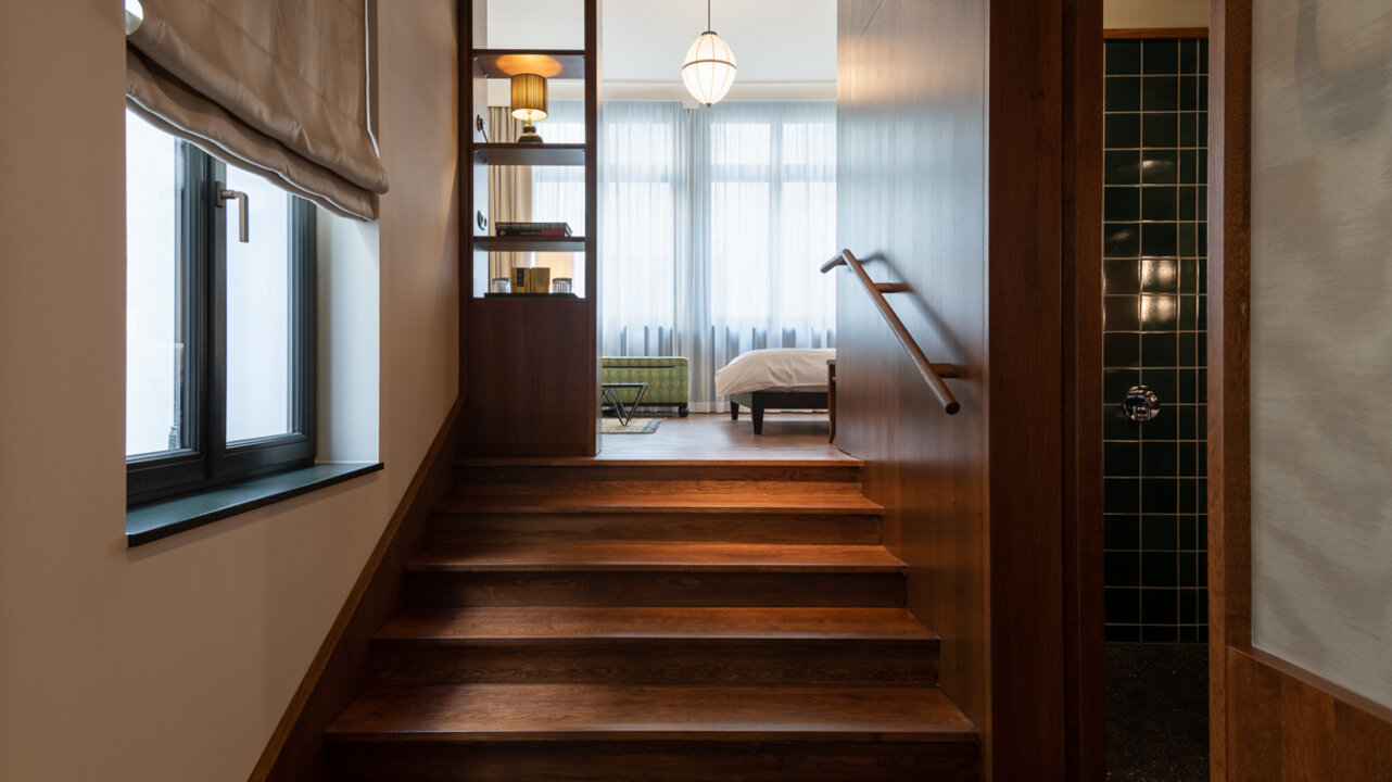 Blick auf die Holztreppe in einem Maisonette-Zimmer des Hotel Château Royal Berlin, der Schlafbereich befindet sich im Hintergrund.