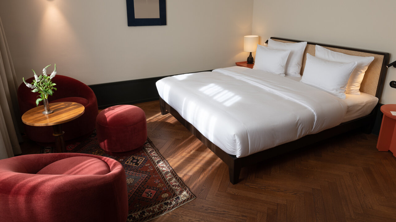 View of a medium-sized hotel room at the Château Royal Berlin with a double bed, a cozy seating area and art by Angela Mewes.