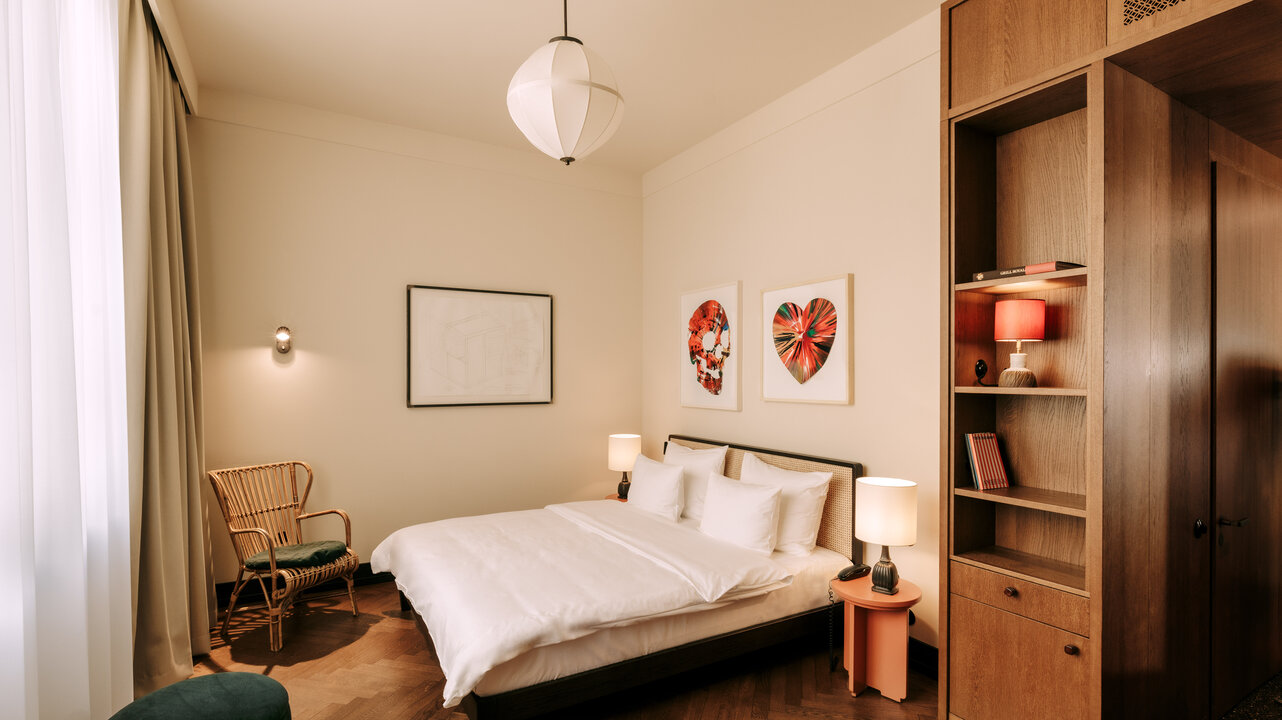 View of a medium hotel room at the Château Royal Berlin with art by Damien Hirst above the bed and a wooden wardrobe.