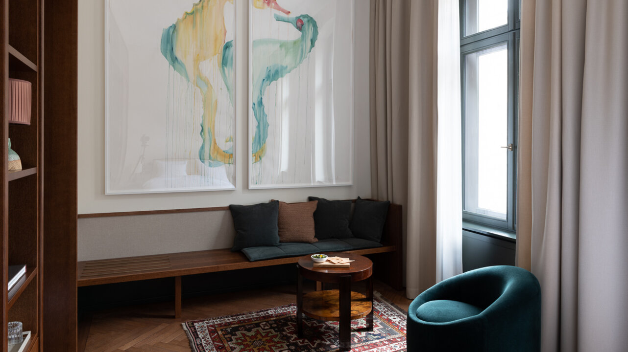 Die Sitzbank in einem Medium-Hotelzimmer des Château Royal Berlin mit einem großen Kunstwerk von Marianna Simnett an der Wand