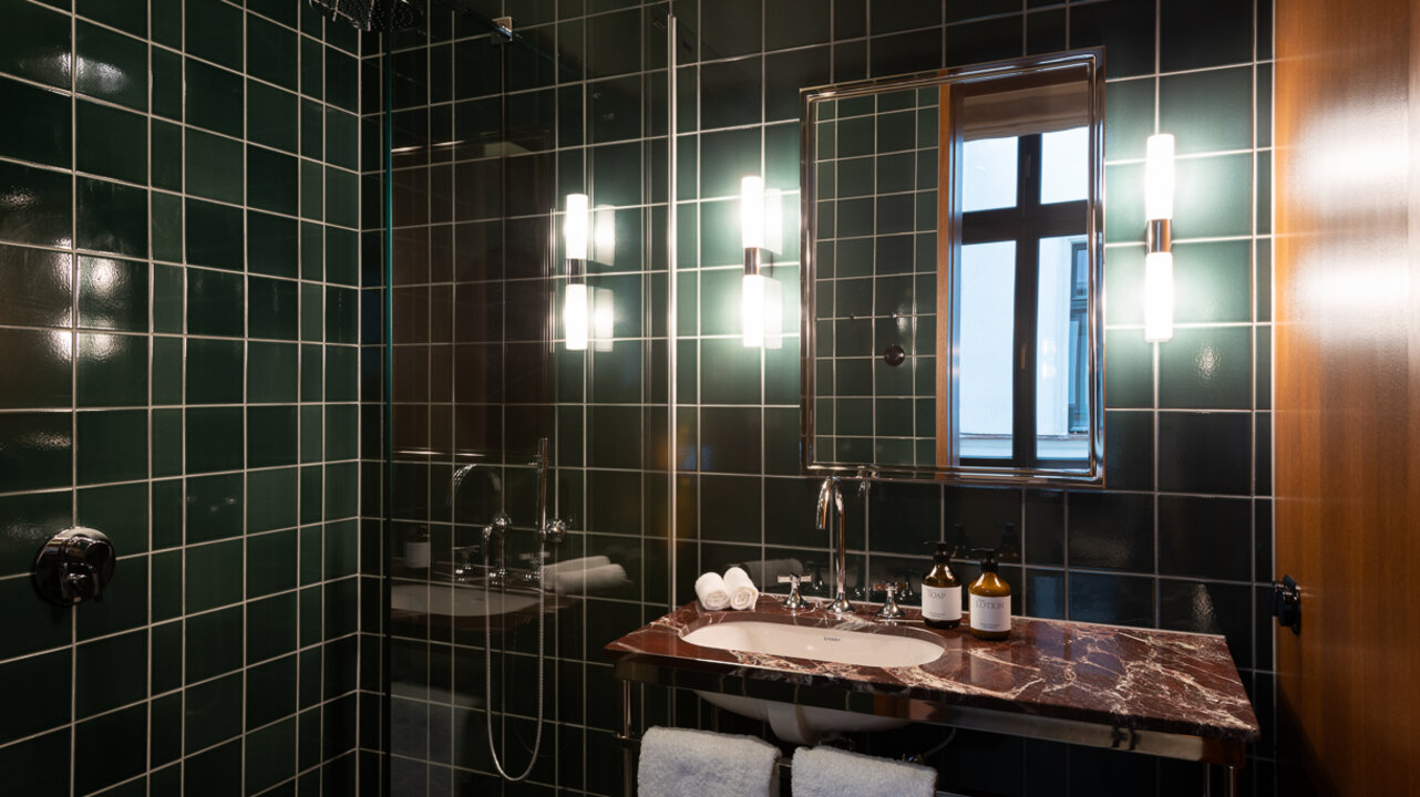 The bathroom with elegant dark tiles in the medium hotel room of the Château Royal with a shower and elegant sink.