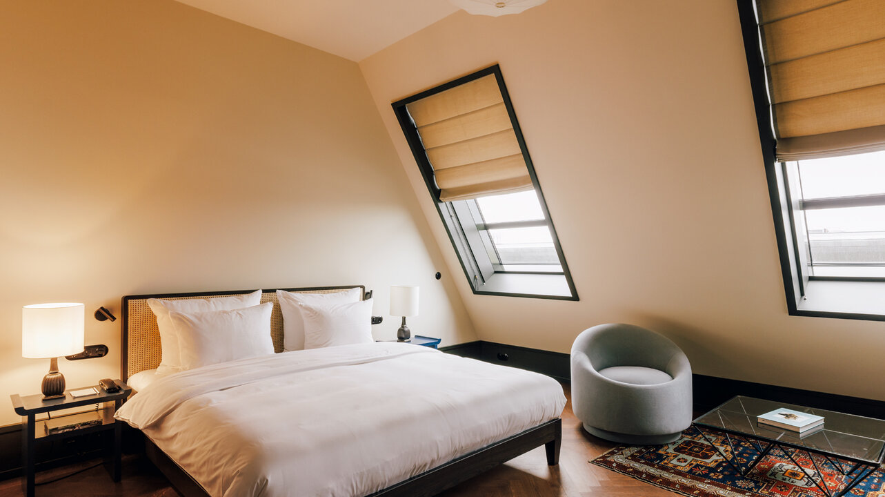 Ansicht des Schlafzimmers mit Dachschräge und einem großen Bett in einem Medium-Hotelzimmer des Château Royal Berlin.