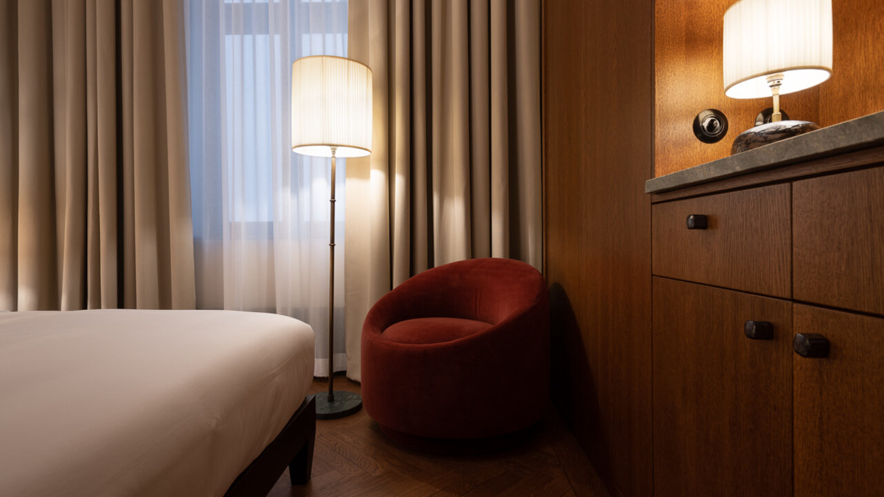 A red armchair between a window and a large wooden cupboard in one of the smaller hotel rooms at the Châteu Royal.