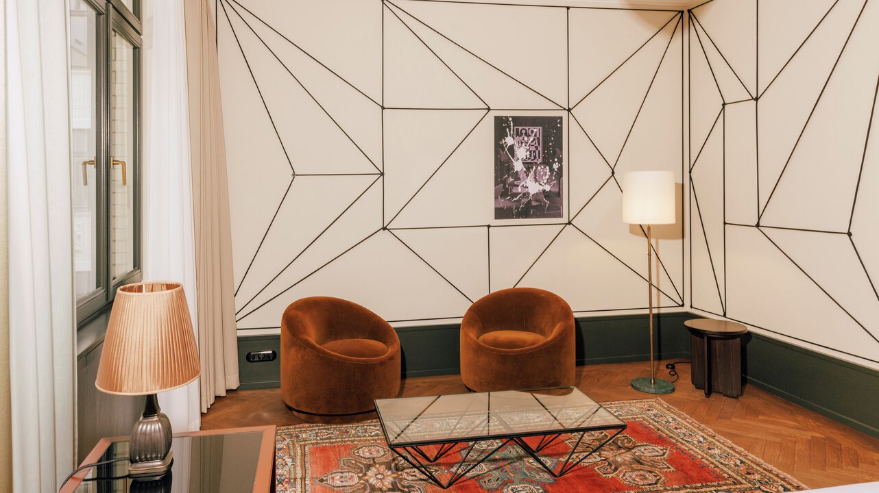 The seating area with a Persian carpet in a junior suite with artwork by Julian Göthe in the Hotel Château Royal Berlin.