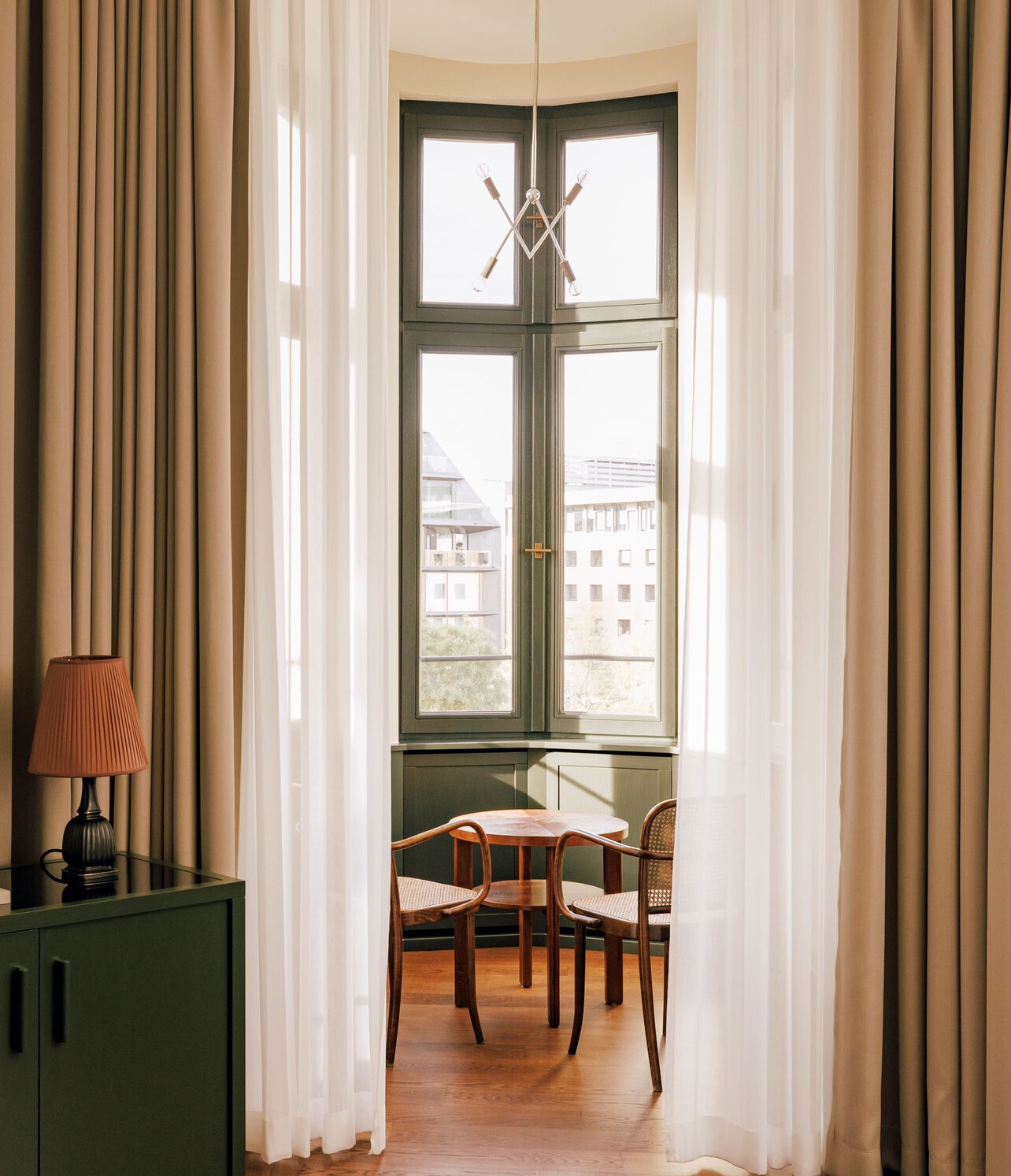 Blick auf den Erker mit gemütlicher Sitzgelegenheit eines in Grün und Beige gestalteten Hotelzimmers im Boutiquehotel Château Royal Berlin