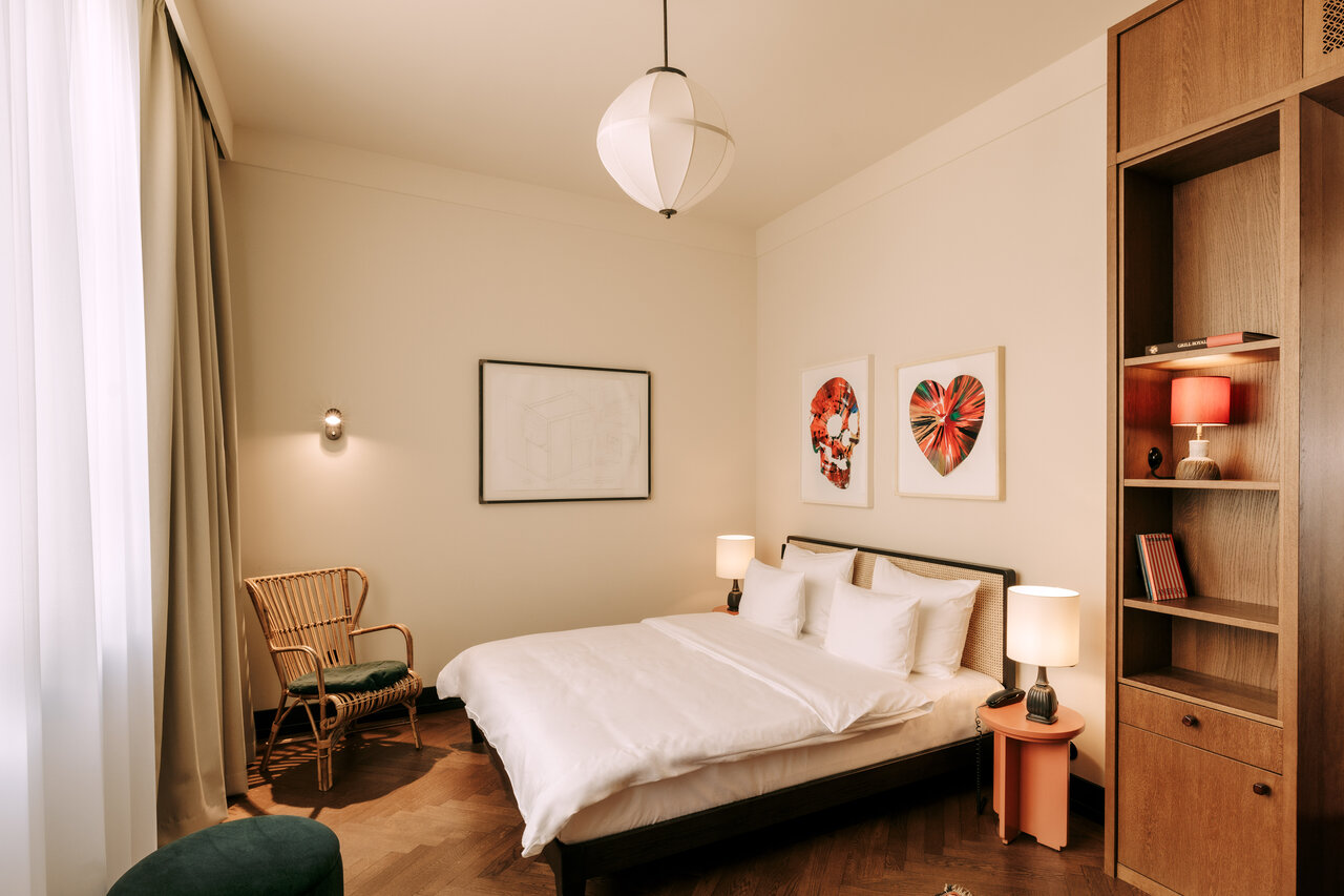 Blick auf das Doppelbett in einem hell gestalteten und mit verschiedenen Kunstwerken ausgestatteten Hotelzimmer des Boutiquehotels Château Royal Berlin